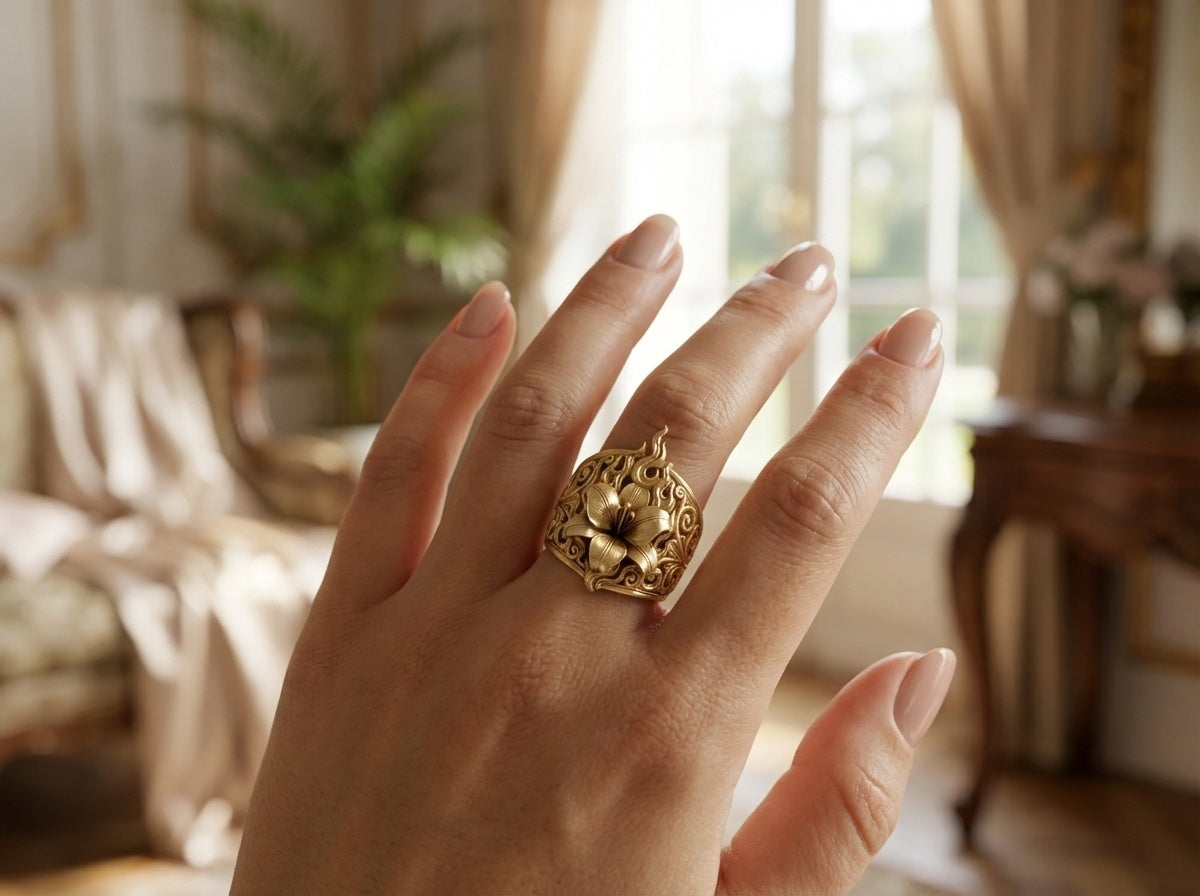Hand wearing a gold lily zolthaire ring with a decorative design in a softly blurred indoor setting